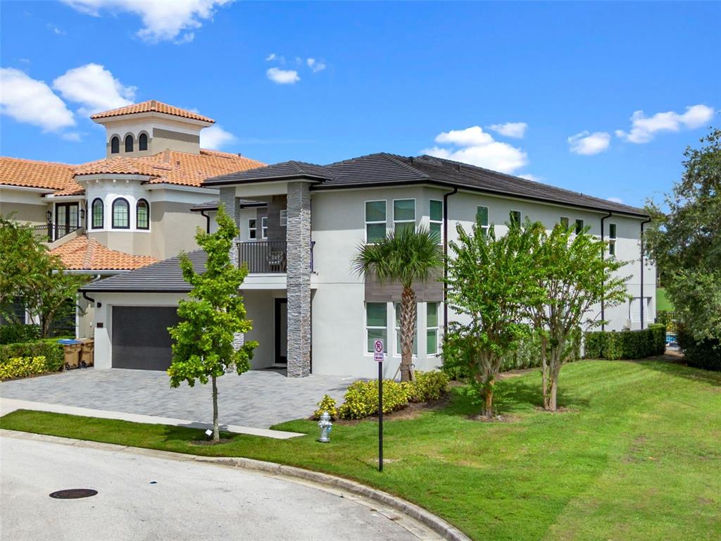 A two-story house with a gray garage, stone accents, and a balcony under a blue sky — 7864 PALMILLA COURT, REUNION, FL