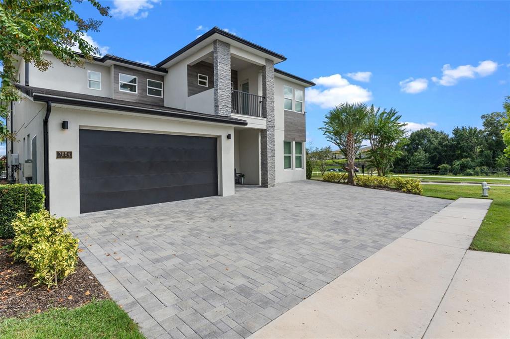 A two-story house features a paved driveway, a dark garage door, and stone accents — 7864 PALMILLA COURT, REUNION, FL
