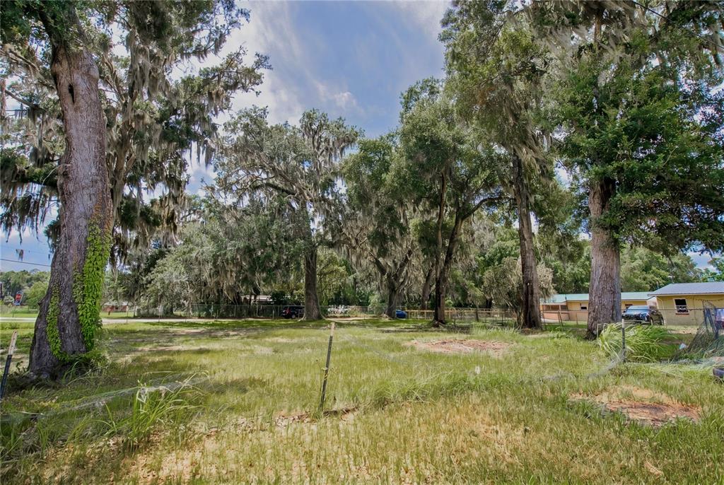 A grassy, fenced lot features several large, moss-draped oak trees under a partly cloudy sky — 720 HUNTINGTON ROAD, CRESCENT CITY, FL