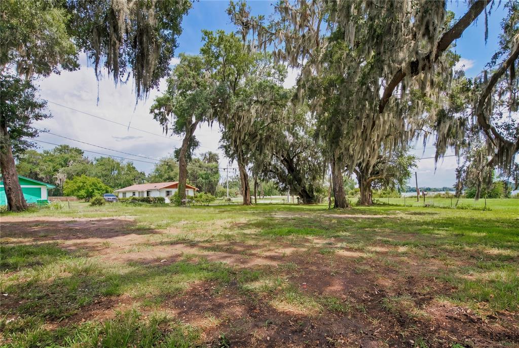 A grassy lot features large, moss-draped oak trees and a house in the background — 720 HUNTINGTON ROAD, CRESCENT CITY, FL