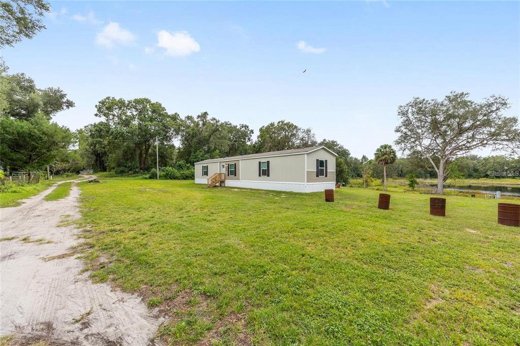 A single-story manufactured home sits on a grassy lot next to a dirt driveway — 14642 NE 111TH TERRACE, FORT MC COY, FL
