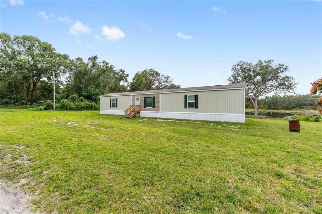 A manufactured home sits on a grassy lot near a pond and wooded area — 14642 NE 111TH TERRACE, FORT MC COY, FL