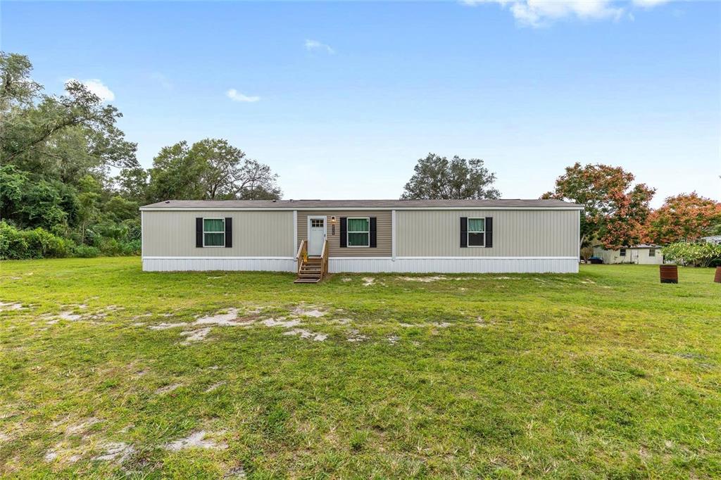 A single-story manufactured home with light siding sits on a large, grassy lot — 14642 NE 111TH TERRACE, FORT MC COY, FL
