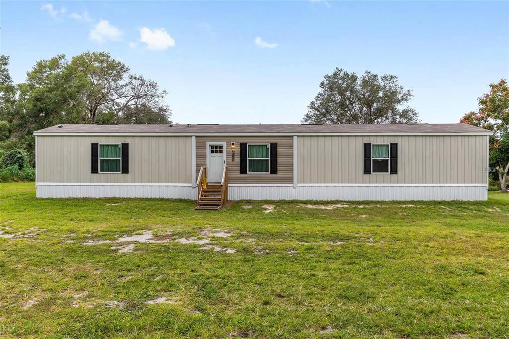 A single-story manufactured home with tan siding and a central entrance sits on a grassy lot — 14642 NE 111TH TERRACE, FORT MC COY, FL