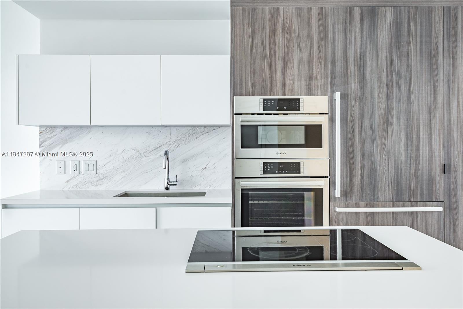 A modern kitchen features white cabinetry, marble backsplash, stainless steel appliances, and a central island — 851 NE 1st Ave # 2100, Miami FL 33132, MIAMI, FL