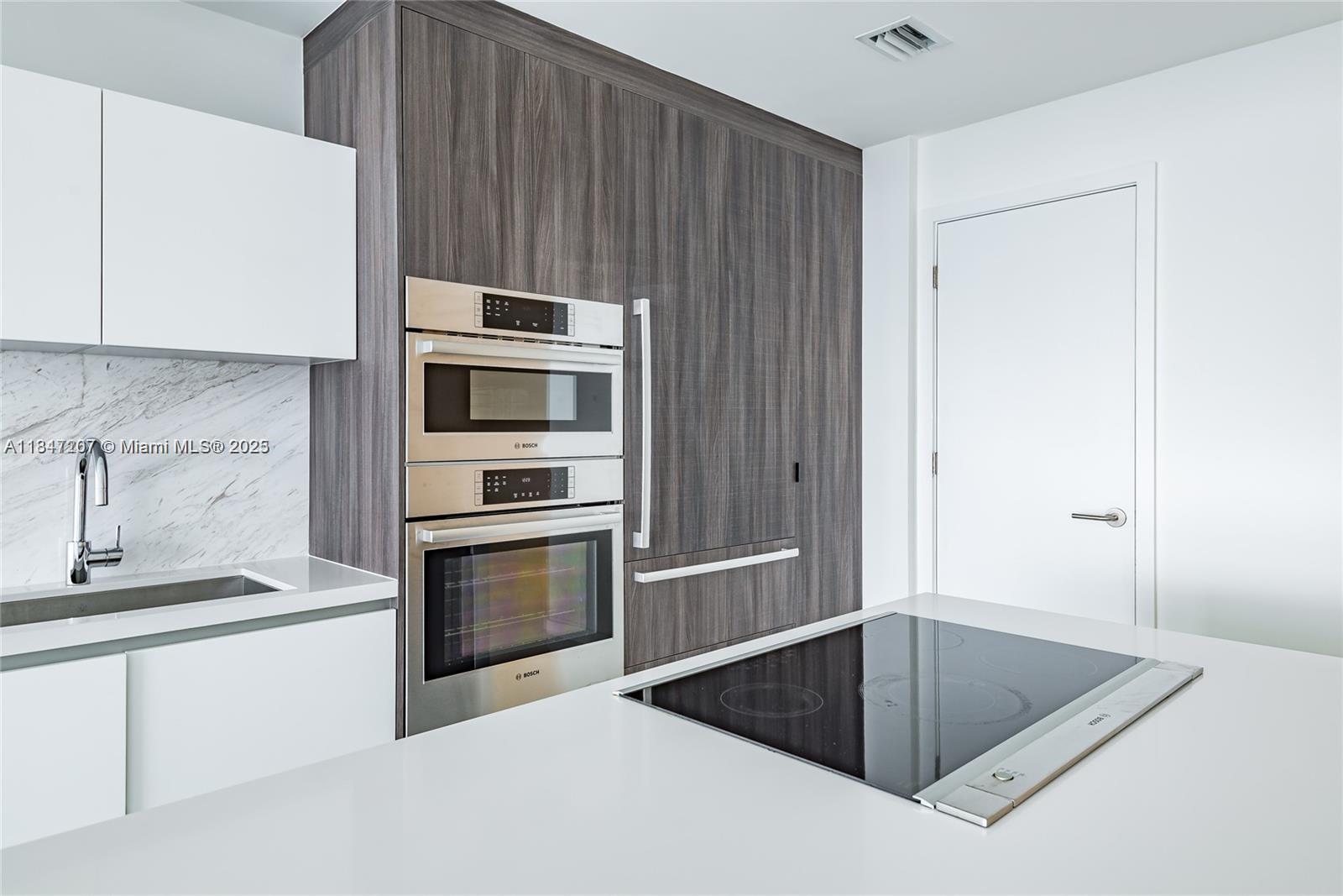 A modern kitchen features white cabinets, marble backsplash, stainless steel appliances, and a dark wood-paneled wall — 851 NE 1st Ave # 2100, Miami FL 33132, MIAMI, FL