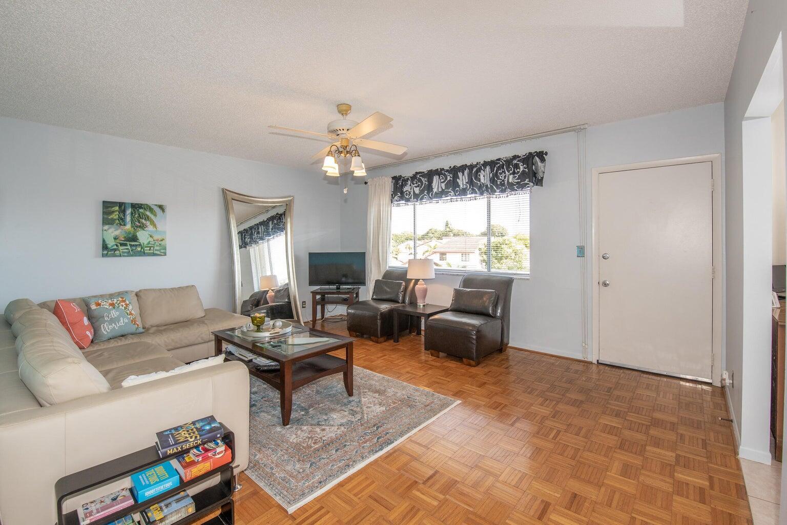 A living room with light blue walls, parquet wood flooring, a sectional sofa, and a window — 6289 Lear Drive # 301, Lake Worth FL 33462, LAKE WORTH, FL