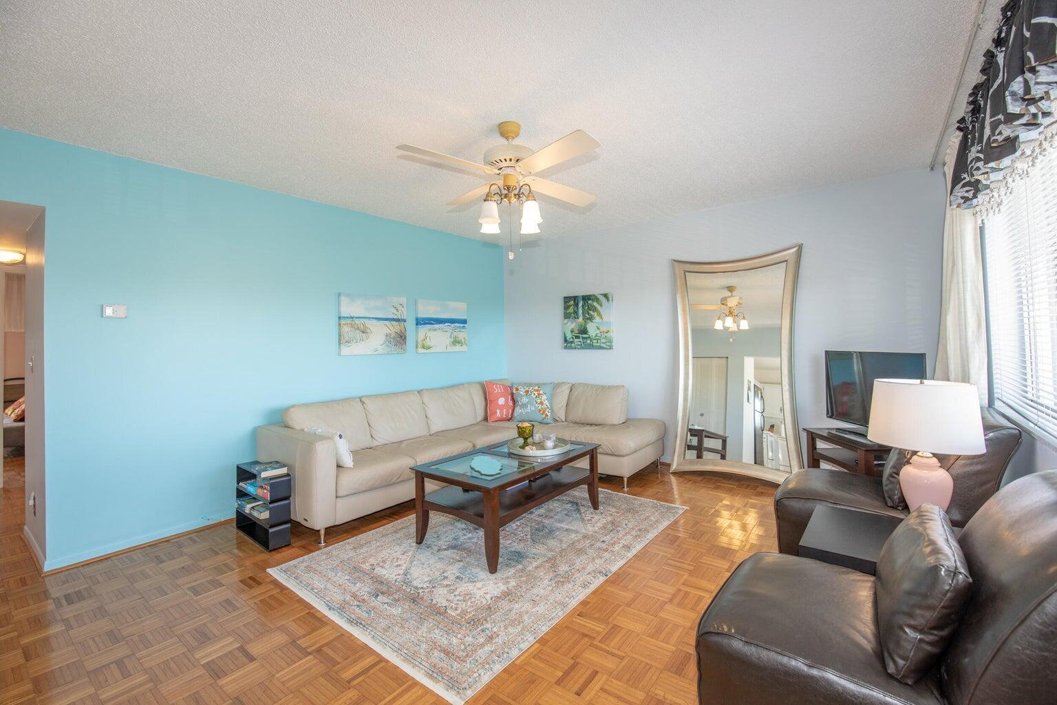 A living room with light blue walls, a beige sectional, leather chairs, and parquet flooring — 6289 Lear Drive # 301, Lake Worth FL 33462, LAKE WORTH, FL