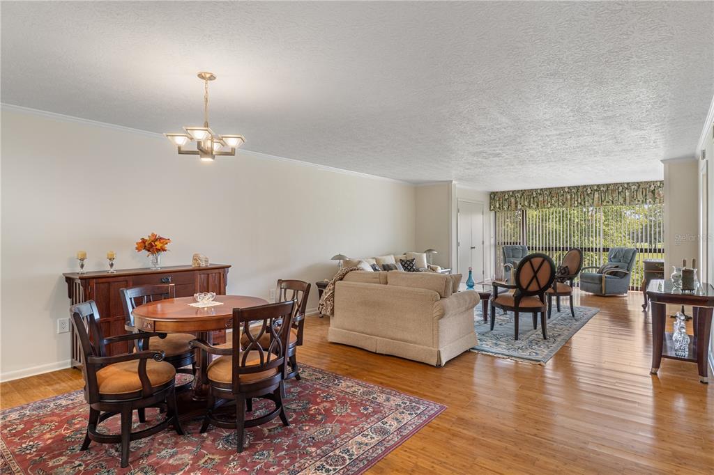 An open-concept living and dining room with hardwood floors, a chandelier, and large windows — 3 CYPRESS RUN UNIT 33C, HOMOSASSA, FL