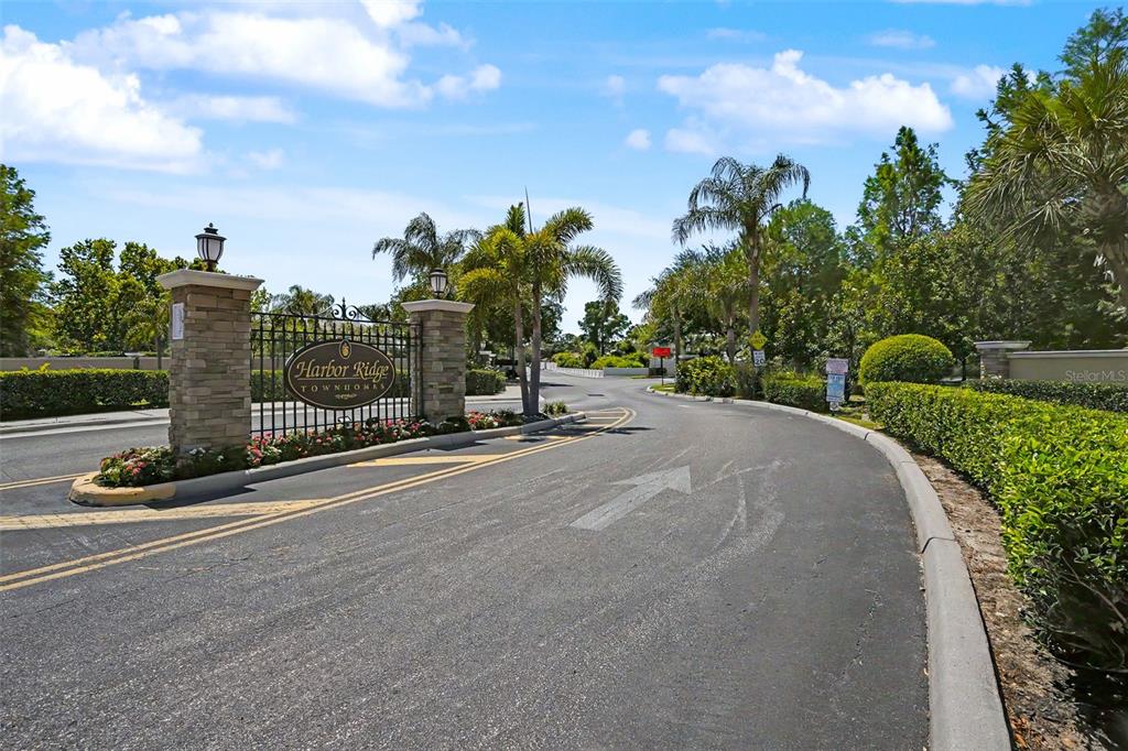 The entrance to Harbor Ridge Townhomes features stone pillars, a metal gate, and landscaping — 441 HARBOR RIDGE DRIVE, PALM HARBOR, FL