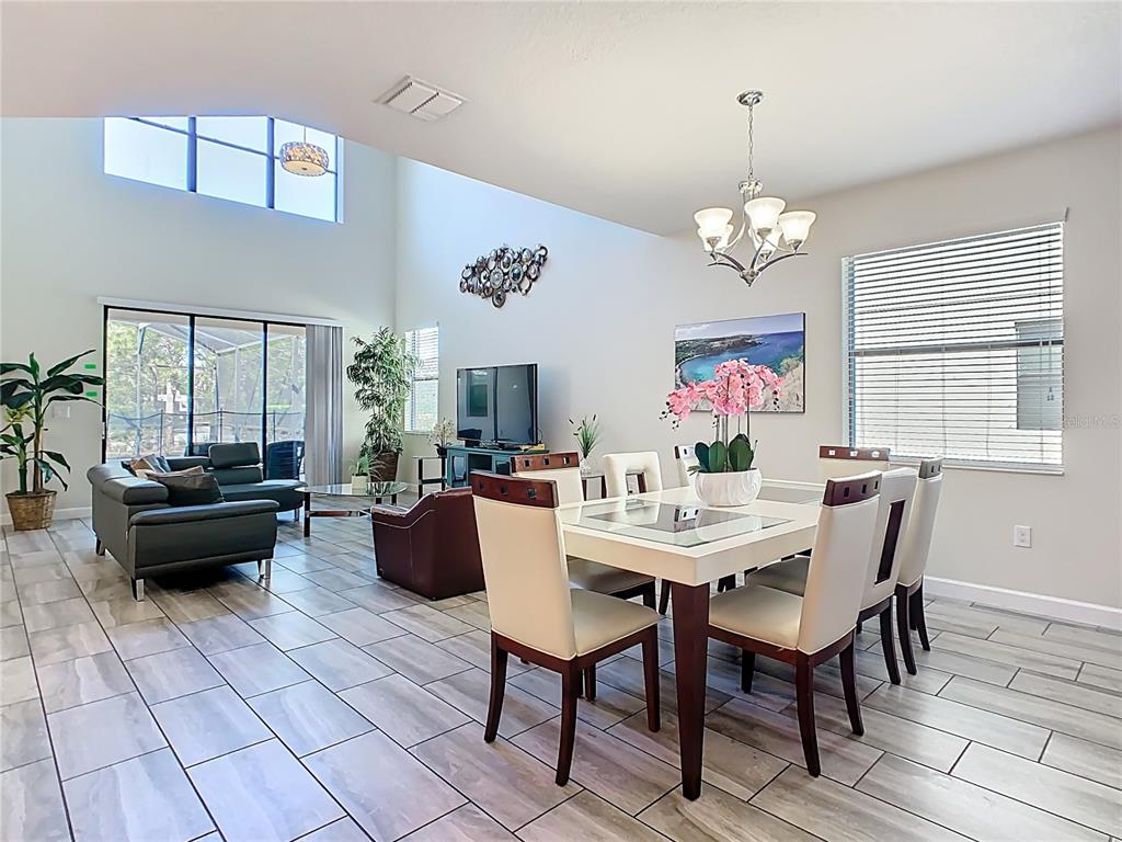 A bright, open-concept dining and living area features high ceilings, tile flooring, and large windows — 5528 SOLTERRA CIRCLE, DAVENPORT, FL