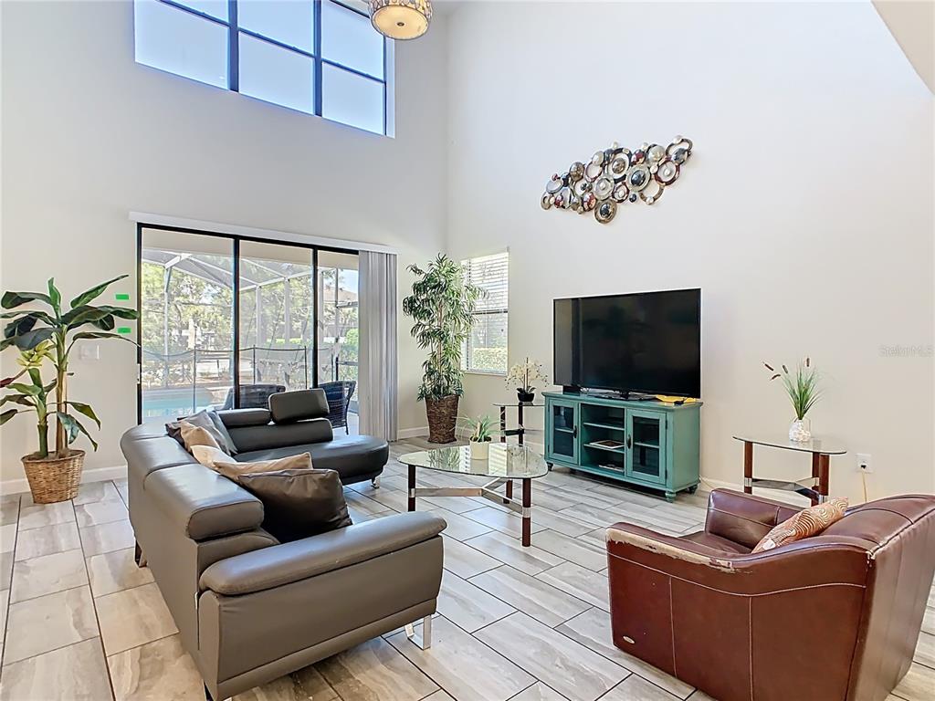 A living room with high ceilings, tile floors, a sectional sofa, and a television console — 5528 SOLTERRA CIRCLE, DAVENPORT, FL
