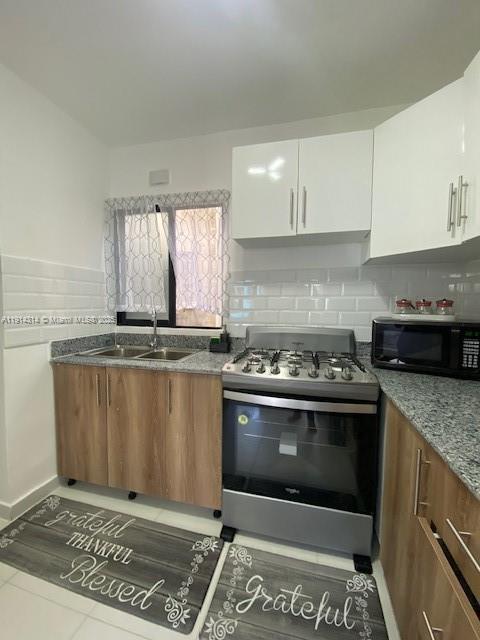A kitchen features wood-toned lower cabinets, white upper cabinets, a gas range, and subway tile — 0 Avenida la Gaviota # 403, NY 11503, NY