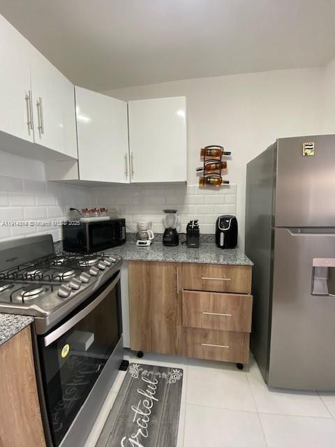A kitchen features white upper cabinets, wood-tone lower cabinets, stainless steel appliances, and subway tile backsplash — 0 Avenida la Gaviota # 403, NY 11503, NY