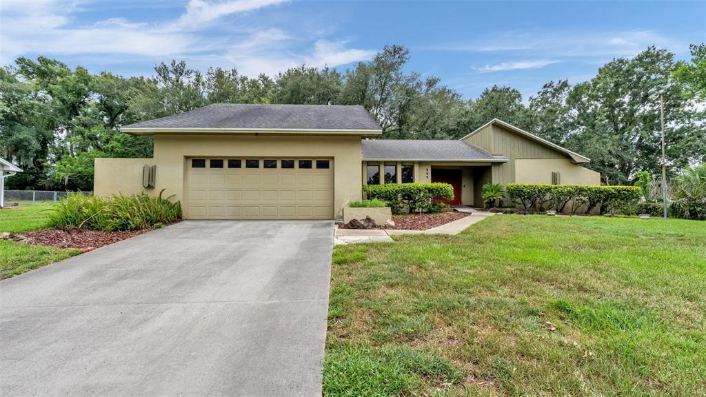 A single-story house with a tan stucco exterior, a two-car garage, and a large lawn — 717 WOODHILL DRIVE, LAKELAND, FL