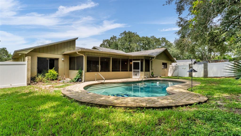 A backyard features a kidney-shaped swimming pool with a paver deck beside a single-story house — 717 WOODHILL DRIVE, LAKELAND, FL