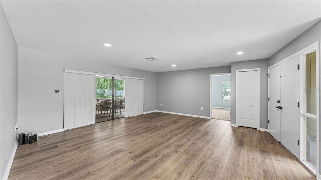 An empty living room with gray walls, wood-look flooring, recessed lighting, and a sliding glass door — 717 WOODHILL DRIVE, LAKELAND, FL