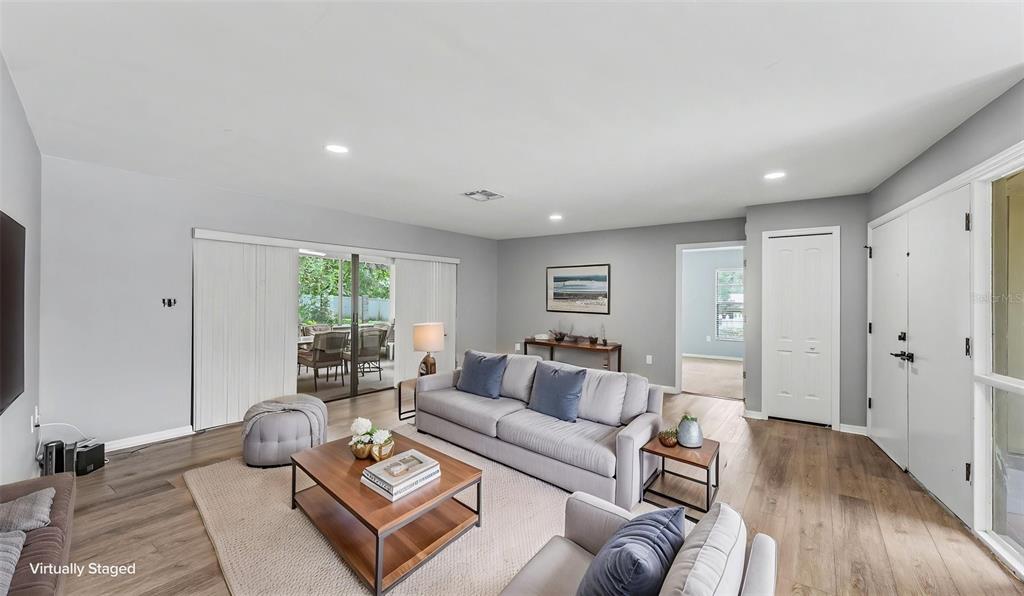 A living room with light gray walls, wood-look flooring, a sofa, and sliding glass doors — 717 WOODHILL DRIVE, LAKELAND, FL