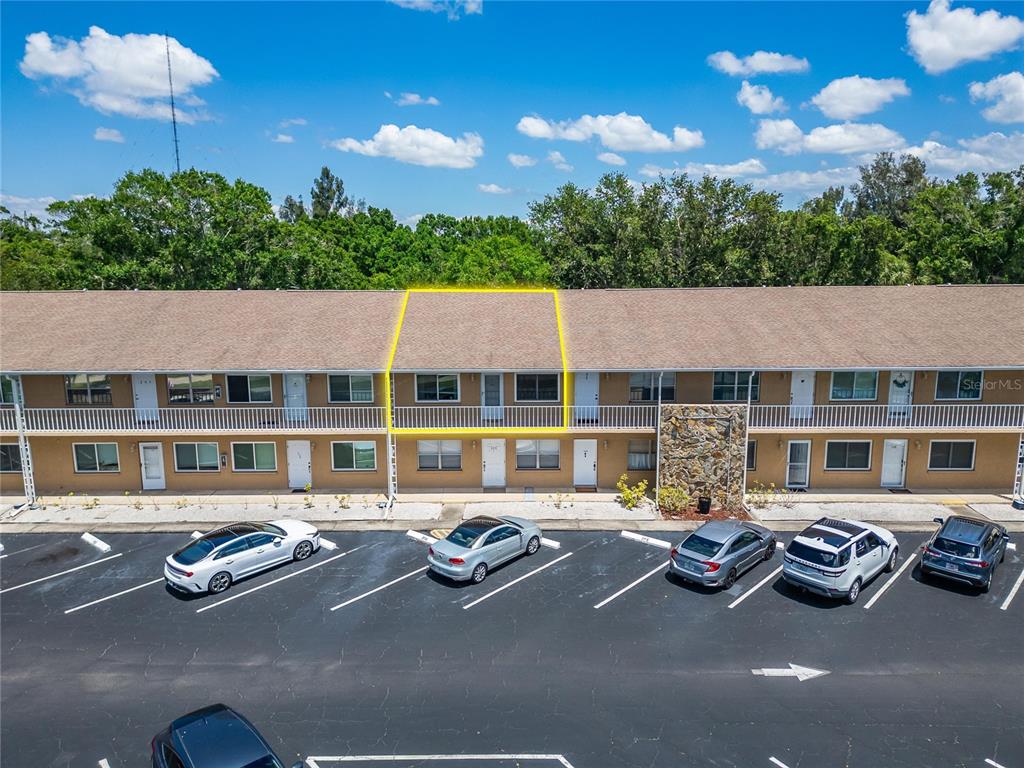 An aerial view shows a long, multi-story apartment building with a parking lot and pool — 8039 GARDEN DRIVE UNIT 205, SEMINOLE, FL