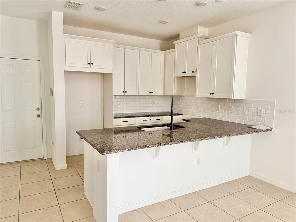A kitchen features white cabinets, granite countertops, a subway tile backsplash, and tile flooring — 9987 RANDAL WALK STREET, ORLANDO, FL