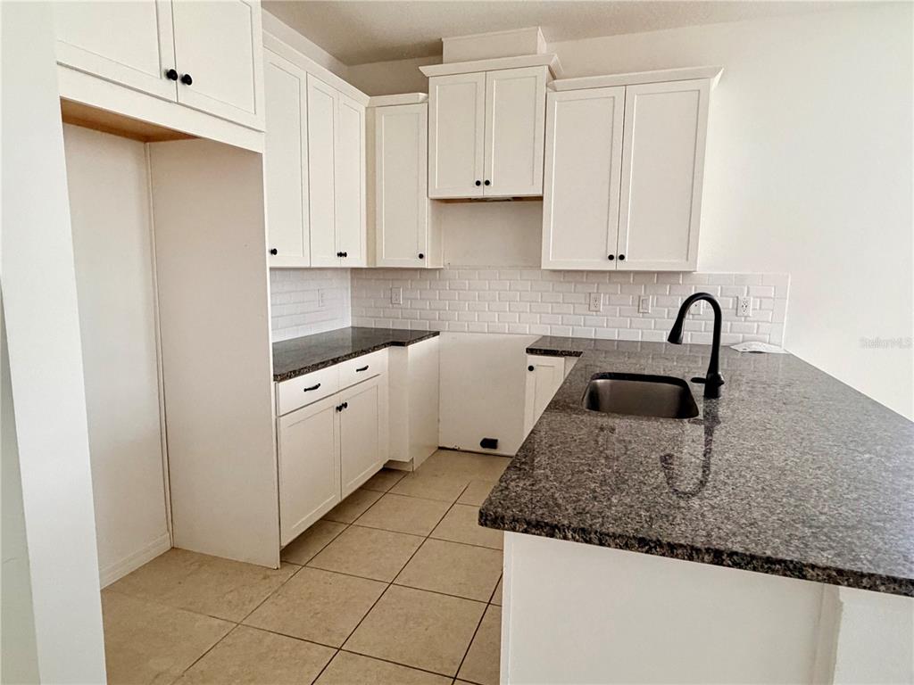 A kitchen features white cabinets, dark granite countertops, a subway tile backsplash, and tile flooring — 9987 RANDAL WALK STREET, ORLANDO, FL
