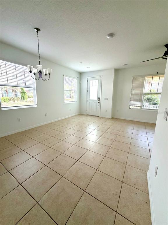 A bright, empty room features beige tile flooring, a chandelier, and a white front door — 9987 RANDAL WALK STREET, ORLANDO, FL