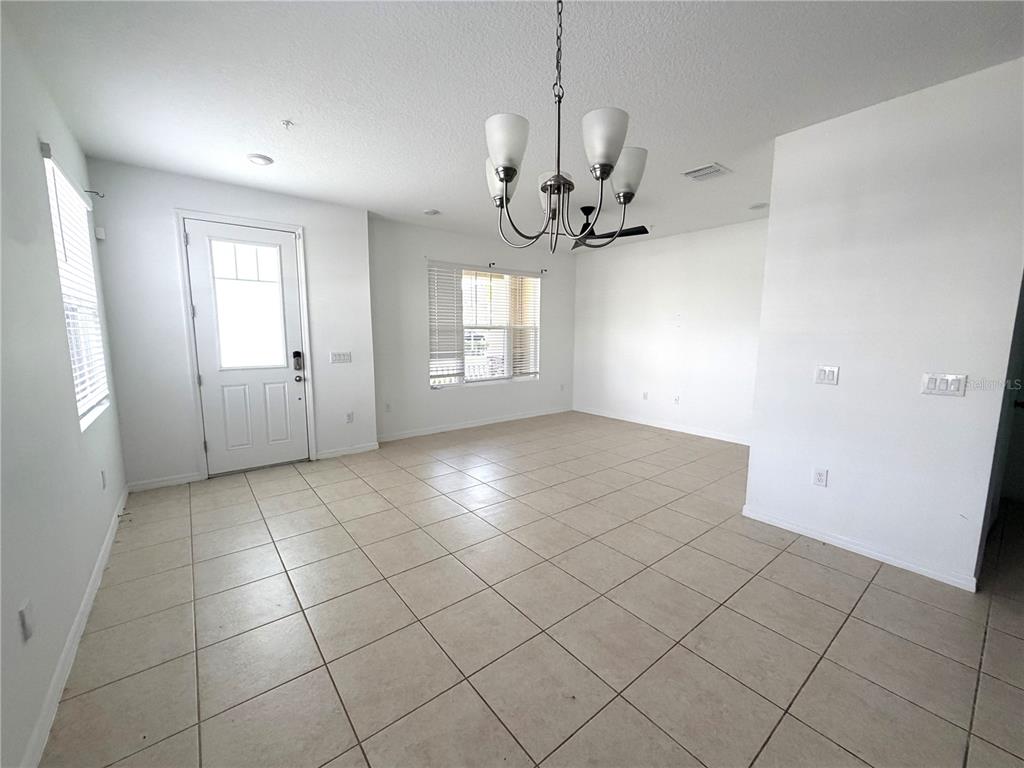 An empty dining area features light-colored tile flooring, a chandelier, and a white exterior door — 9987 RANDAL WALK STREET, ORLANDO, FL