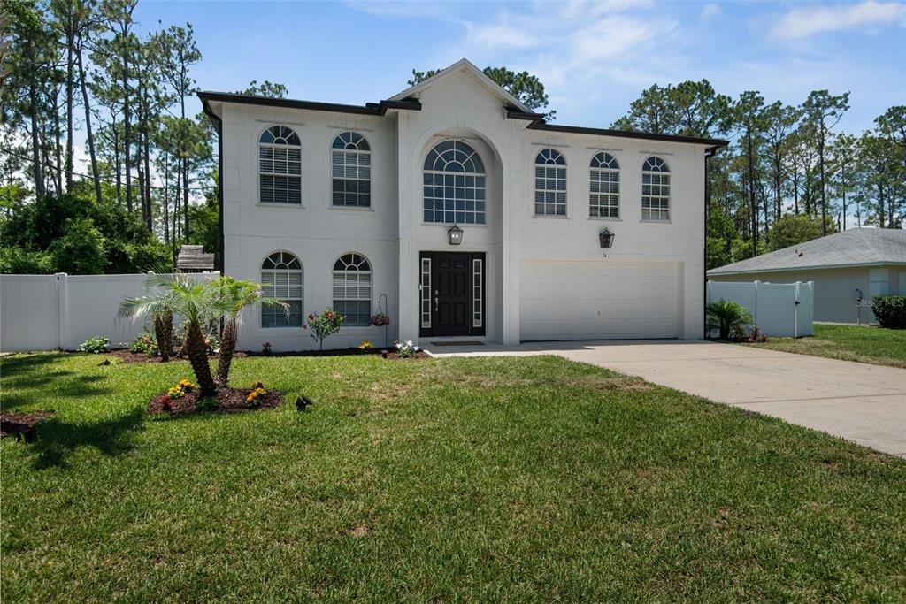 A two-story white house with a two-car garage and arched windows under a blue sky — 14 LLEWELLYN TRAIL, PALM COAST, FL