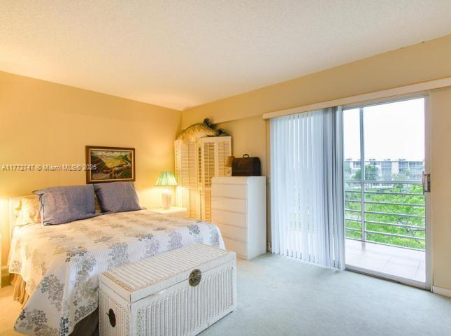 A bedroom features a bed with a white patterned quilt, a wicker chest, and a balcony — 251 Mansfield F # 251F, Boca Raton FL 33434, BOCA RATON, FL