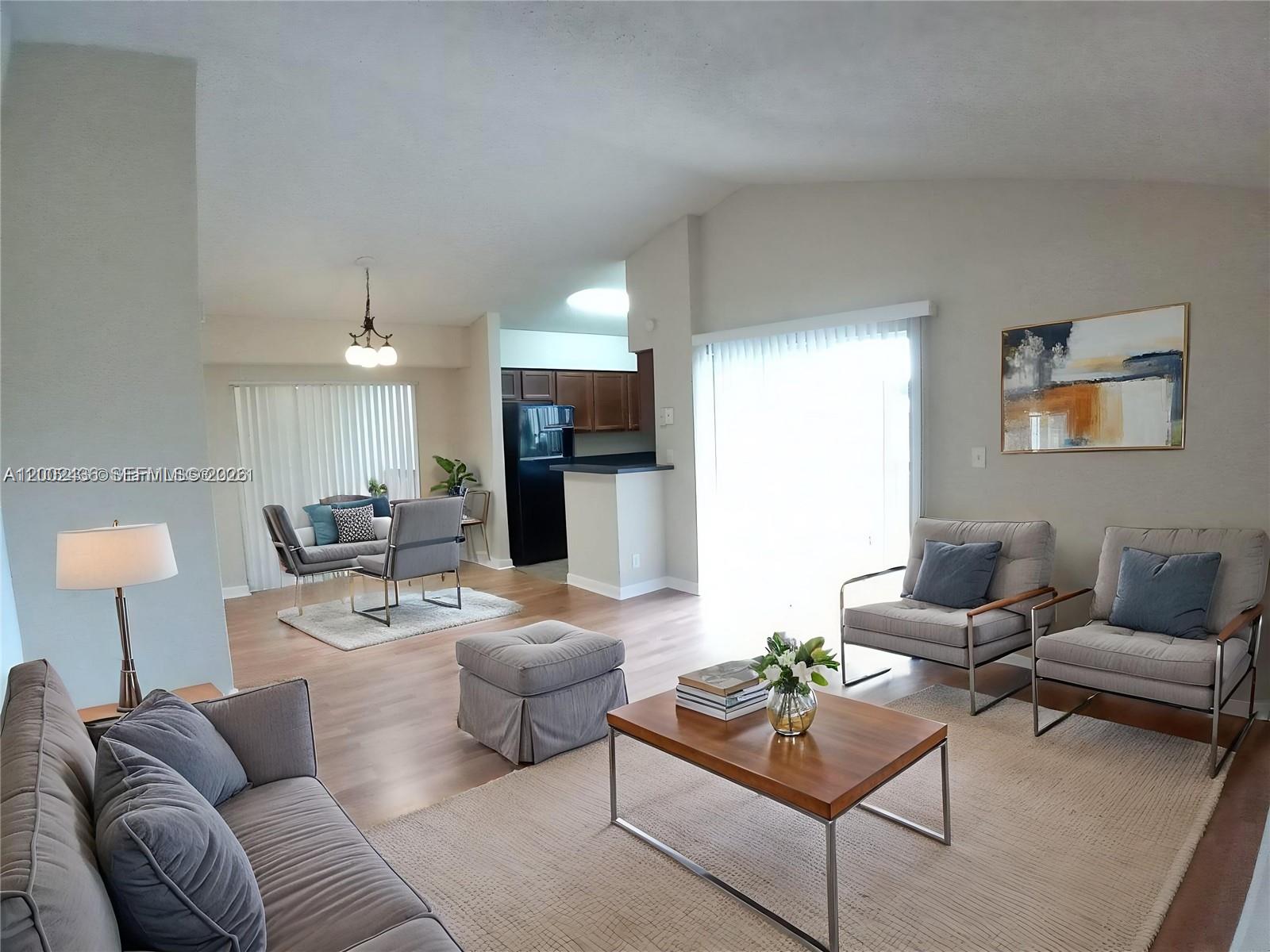 A living room and dining area feature light wood floors, neutral furniture, and a kitchen — TAMARAC, FL