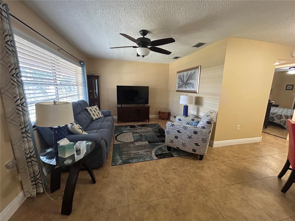 A living room features a blue sofa, patterned armchair, area rug, and a ceiling fan — 10037 62ND TERRACE N UNIT 15, ST PETERSBURG, FL