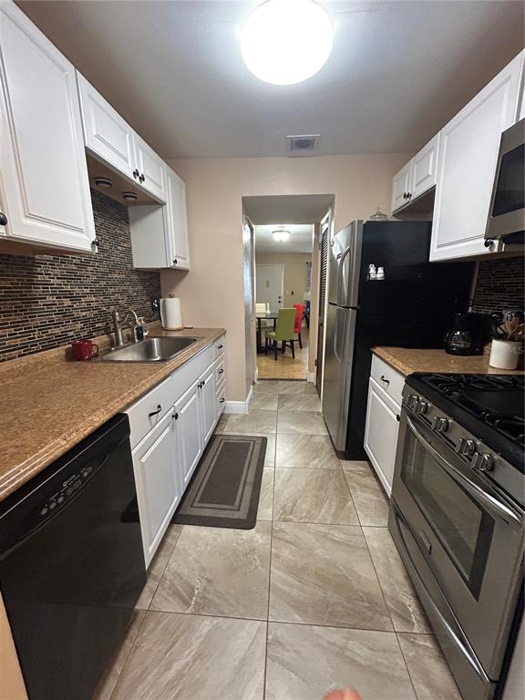 A galley kitchen features white cabinets, stainless steel appliances, and a brown tiled backsplash — 10037 62ND TERRACE N UNIT 15, ST PETERSBURG, FL