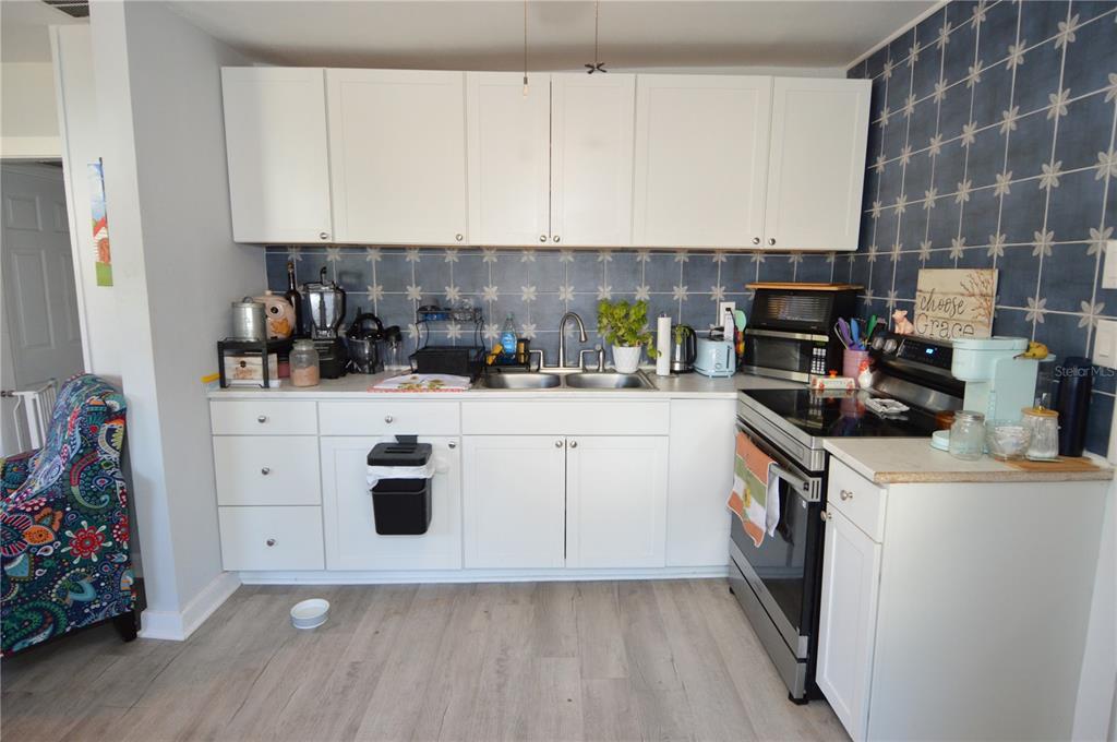 A kitchen features white cabinets, a blue patterned backsplash, stainless steel appliances, and wood flooring — 2852 60TH AVENUE N, ST PETERSBURG, FL