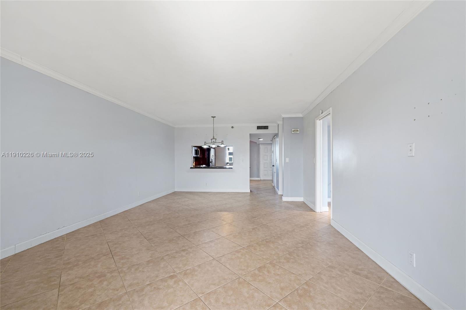 An empty living area features light gray walls, beige tile flooring, and a kitchen pass-through — 2206 S Cypress Bend Dr # 801, Pompano Beach FL 33069, POMPANO BEACH, FL