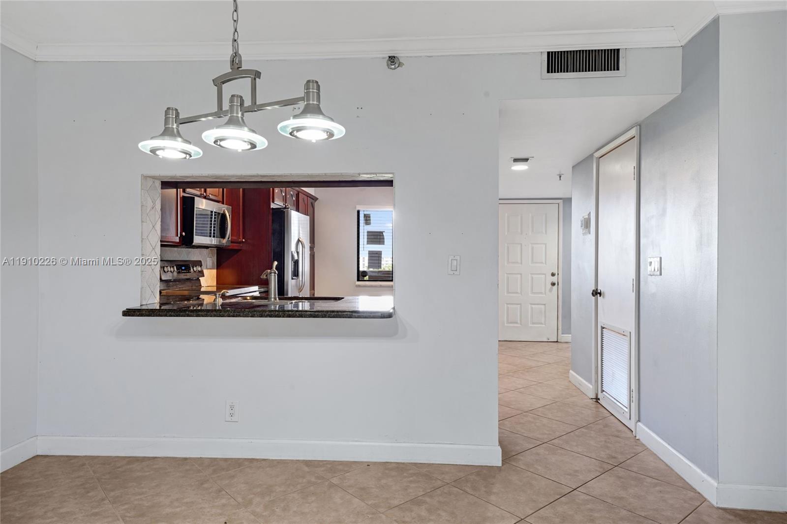 A kitchen pass-through window overlooks a dining area with tile floors and a chandelier — 2206 S Cypress Bend Dr # 801, Pompano Beach FL 33069, POMPANO BEACH, FL