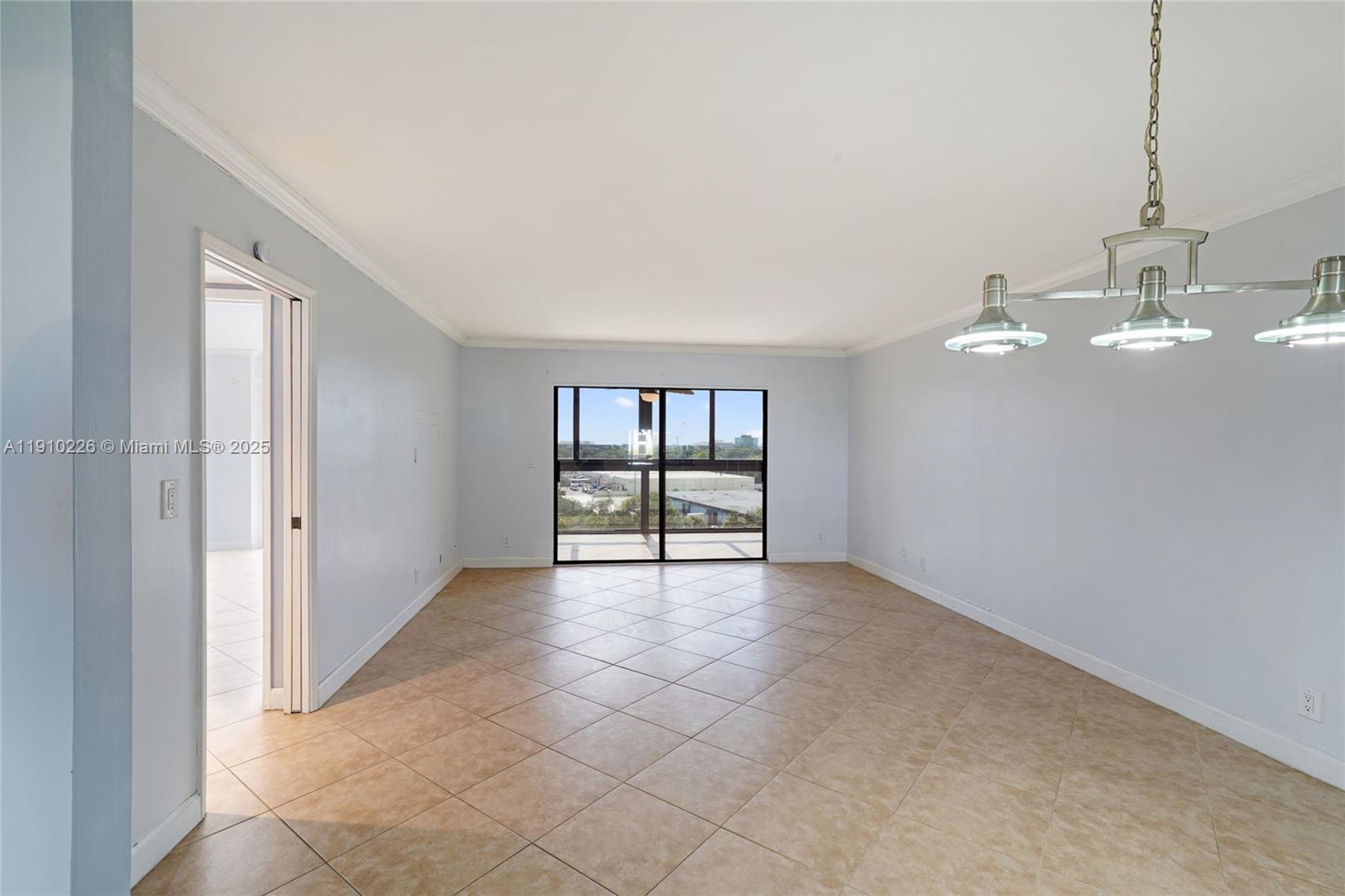 An empty room features light blue walls, beige tile flooring, and a modern pendant light — 2206 S Cypress Bend Dr # 801, Pompano Beach FL 33069, POMPANO BEACH, FL