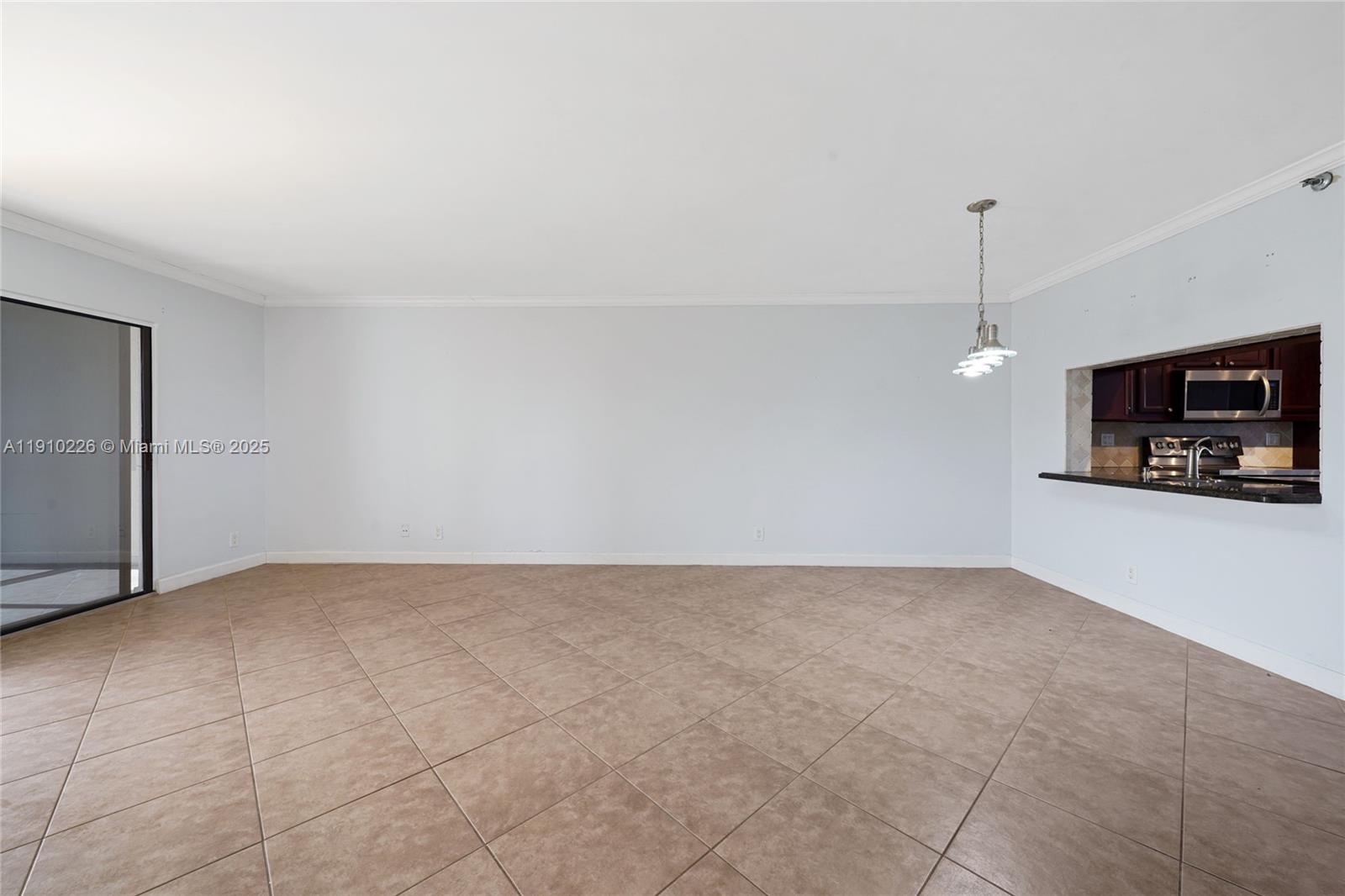 An empty room with beige tile flooring features a kitchen pass-through and sliding glass doors — 2206 S Cypress Bend Dr # 801, Pompano Beach FL 33069, POMPANO BEACH, FL