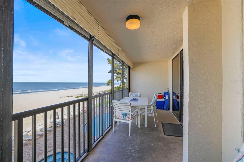 A balcony with a dining set overlooks a beach, ocean, and a swimming pool below — 20040 GULF BOULEVARD UNIT 302, INDIAN SHORES, FL