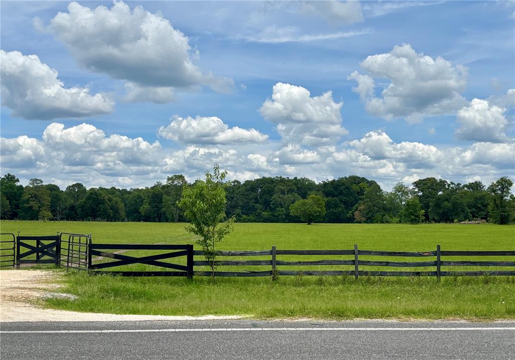 A black wooden fence borders a large green pasture under a blue sky with clouds — NW 202ND STREET, HIGH SPRINGS, FL