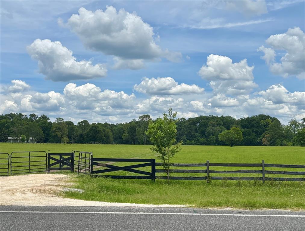 A black wooden fence and gate enclose a large, grassy pasture under a cloudy sky — NW 202ND STREET, HIGH SPRINGS, FL