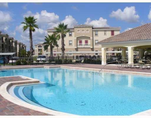 A swimming pool sits in front of a multi-story apartment building with palm trees — 3000 LAUREL PARK LANE UNIT 207, KISSIMMEE, FL