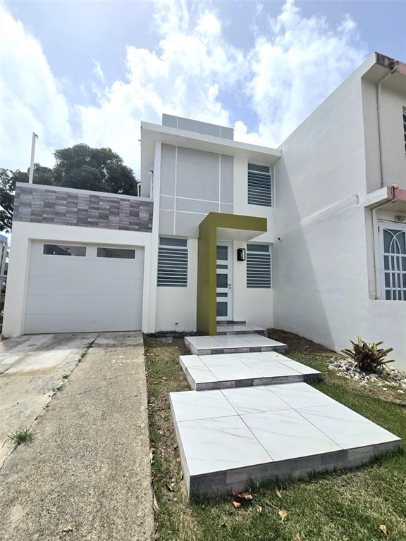 A two-story house exterior features a white garage, tiled walkway, and a green entryway accent — MONTE BRISAS CALLE 2, FAJARDO, PR