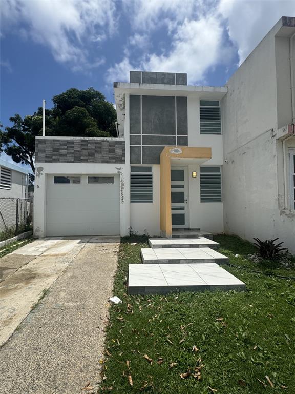 A two-story house features a white garage, a yellow entryway, and a gray tiled facade — MONTE BRISAS CALLE 2, FAJARDO, PR