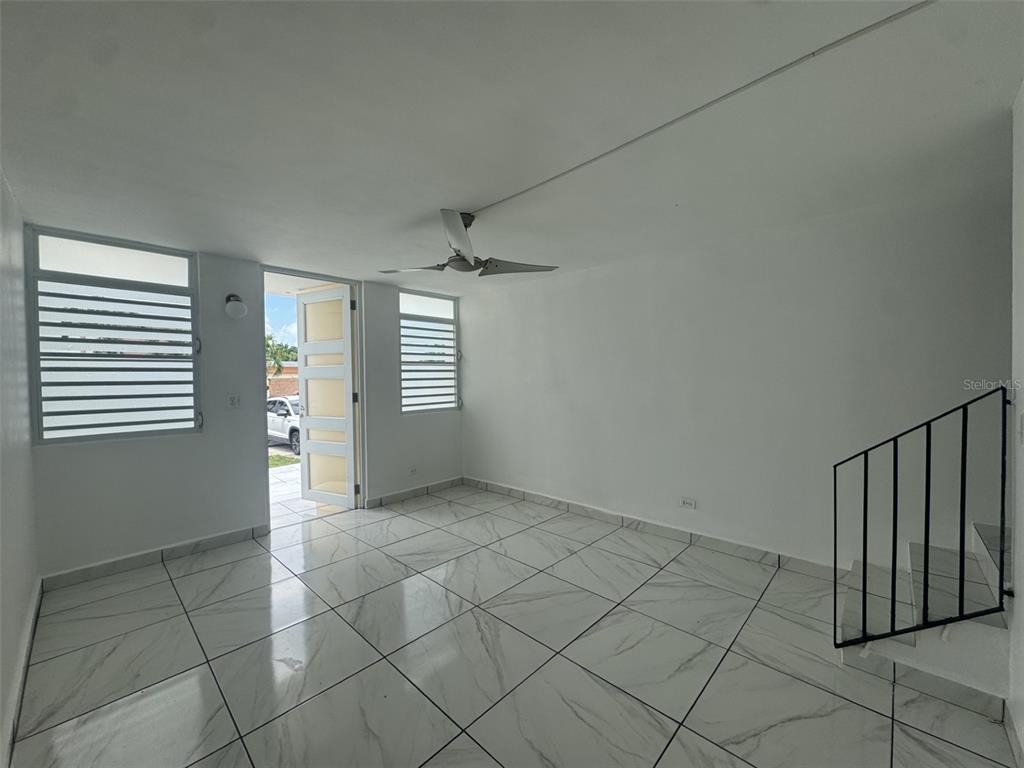 An empty room features white marble-look tile floors, a ceiling fan, and a staircase — MONTE BRISAS CALLE 2, FAJARDO, PR