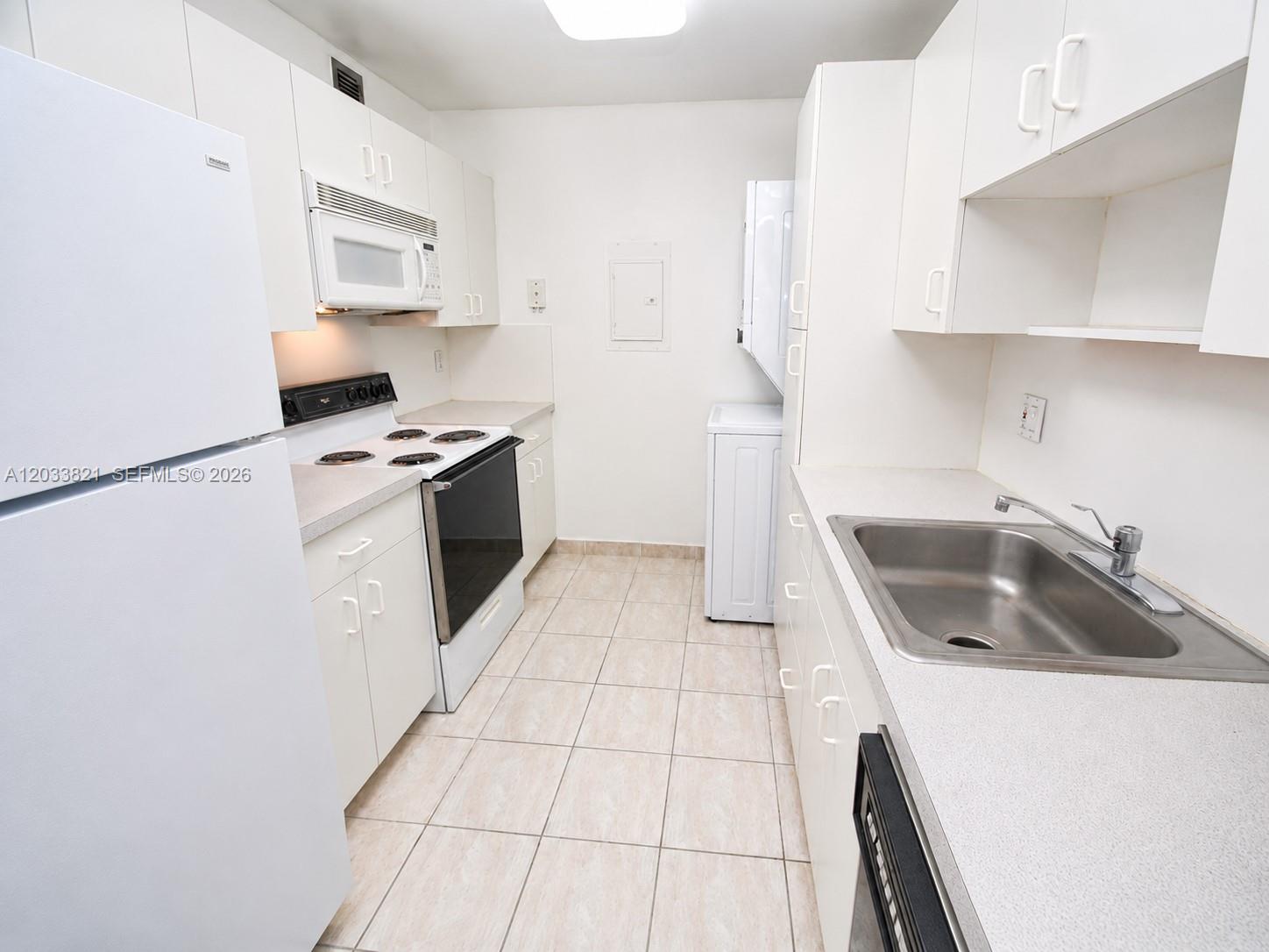 A galley kitchen features white cabinets, white appliances, a stainless steel sink, and tile flooring — 7935 SW 86th St # 823, Miami FL 33143, MIAMI, FL