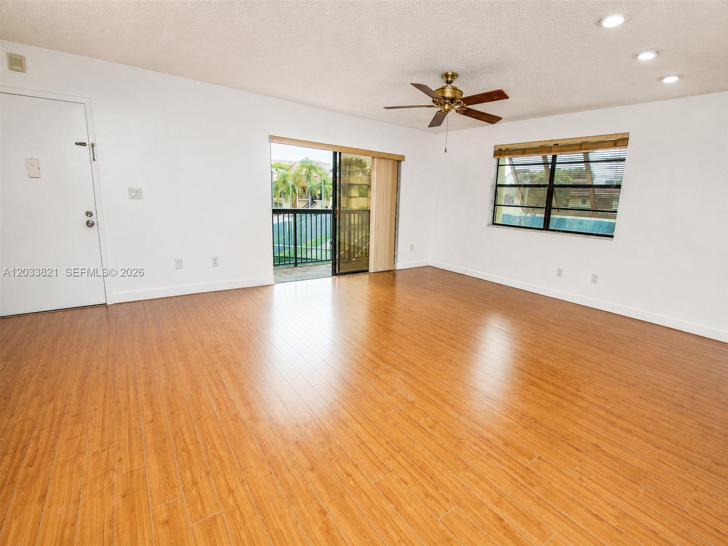 An empty living room features wood-look flooring, a ceiling fan, and a sliding glass door — 7935 SW 86th St # 823, Miami FL 33143, MIAMI, FL