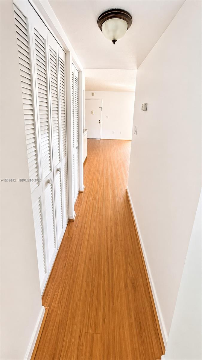 A hallway with wood-look flooring and white louvered closet doors leads to an open room — 7935 SW 86th St # 823, Miami FL 33143, MIAMI, FL
