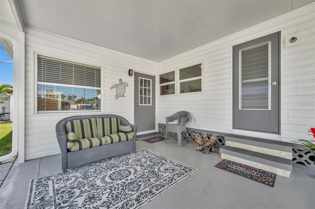 A covered porch features white siding, a grey sofa, a patterned rug, and two grey doors — 247 PALM LANE, PALMETTO, FL