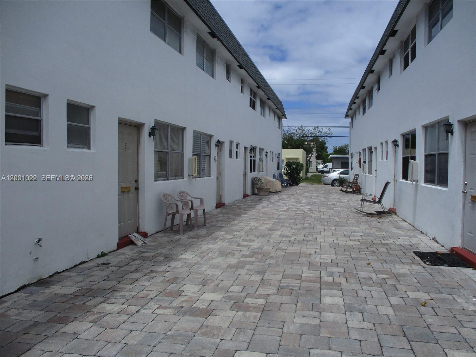 An exterior view shows a paved courtyard between two white apartment buildings with multiple doors — 1949 Taylor St # 9, Hollywood FL 33020, HOLLYWOOD, FL