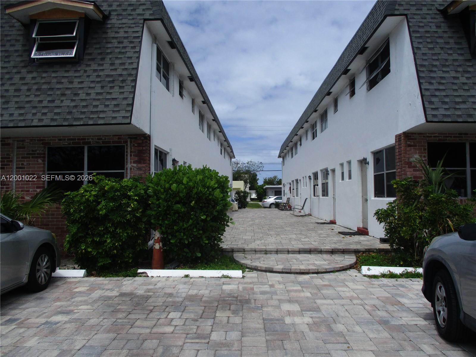 A paved courtyard sits between two white two-story apartment buildings with shingled mansard roofs — 1949 Taylor St # 9, Hollywood FL 33020, HOLLYWOOD, FL